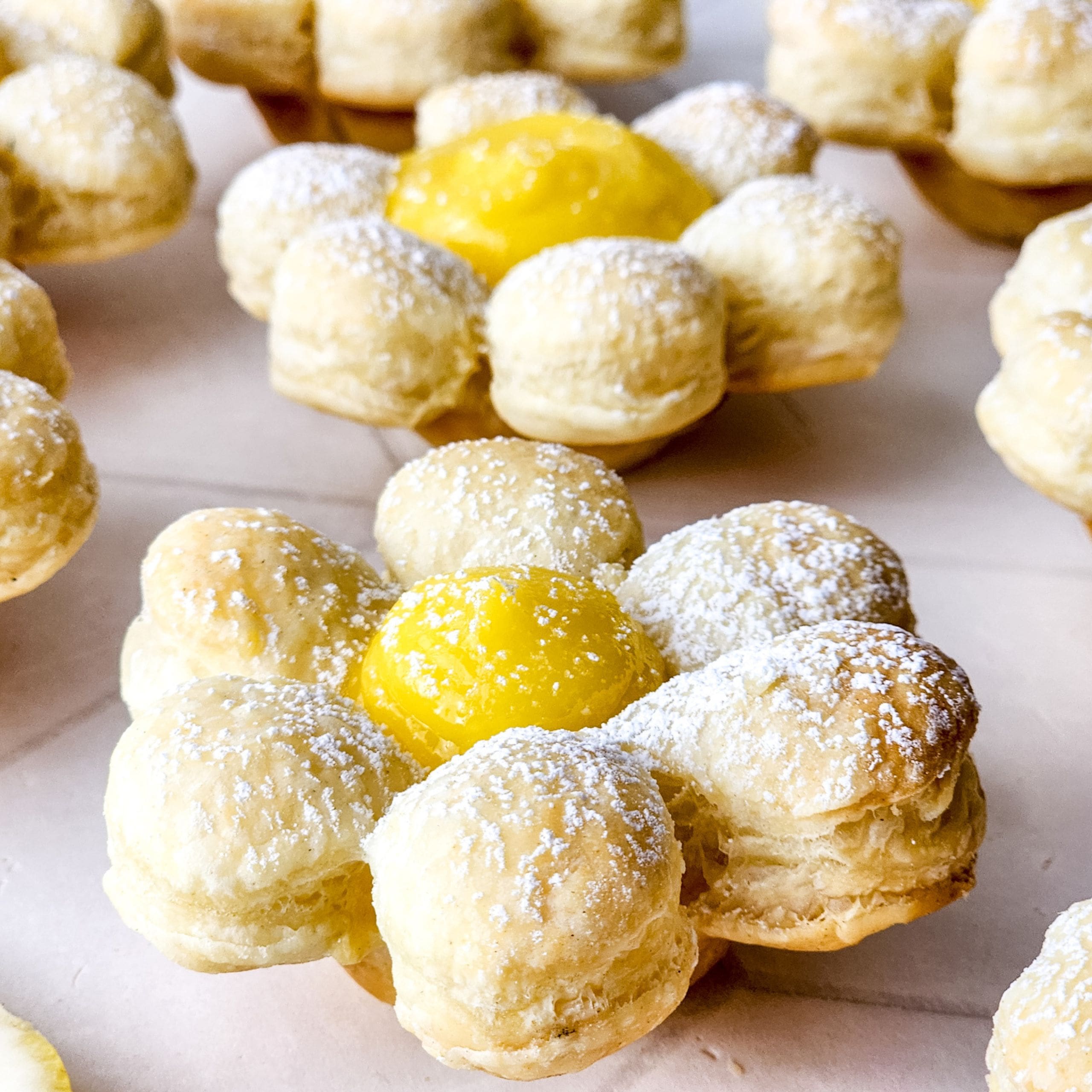 Lemon Flower Cookies: Delicate, flower-shaped puff pastries with powdered sugar and a bright yellow cream center, beautifully arranged on a light surface.