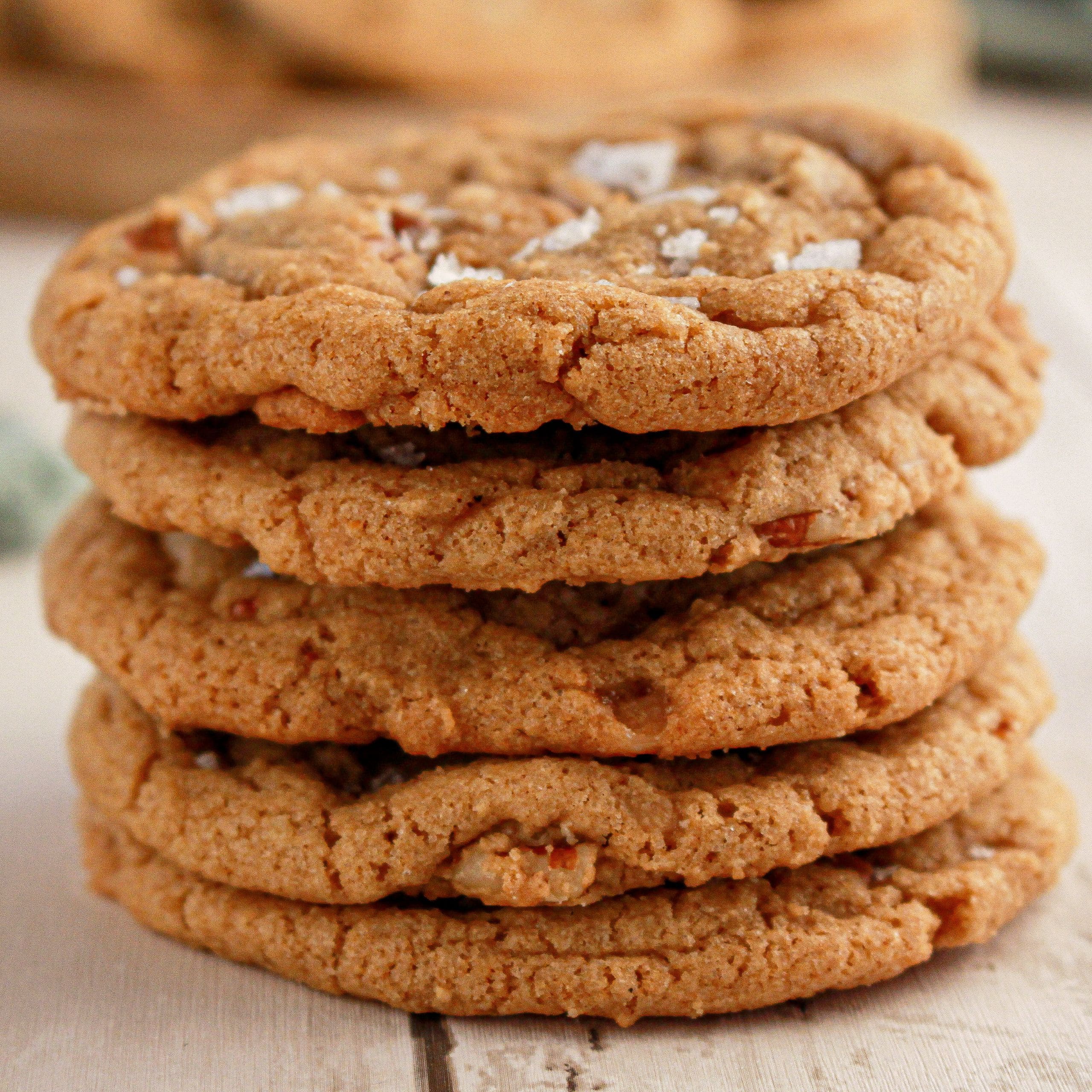 A stack of five pecan toffee cookies with visible oats and sprinkled sea salt on top, placed on a light wooden surface.