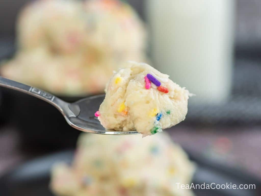 A spoonful of funfetti edible cookie dough with a bowl of cookie dough and milk in the background