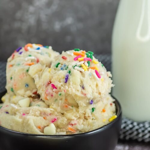 A black bowl with funfetti edible cookie dough with carafe of milk in background