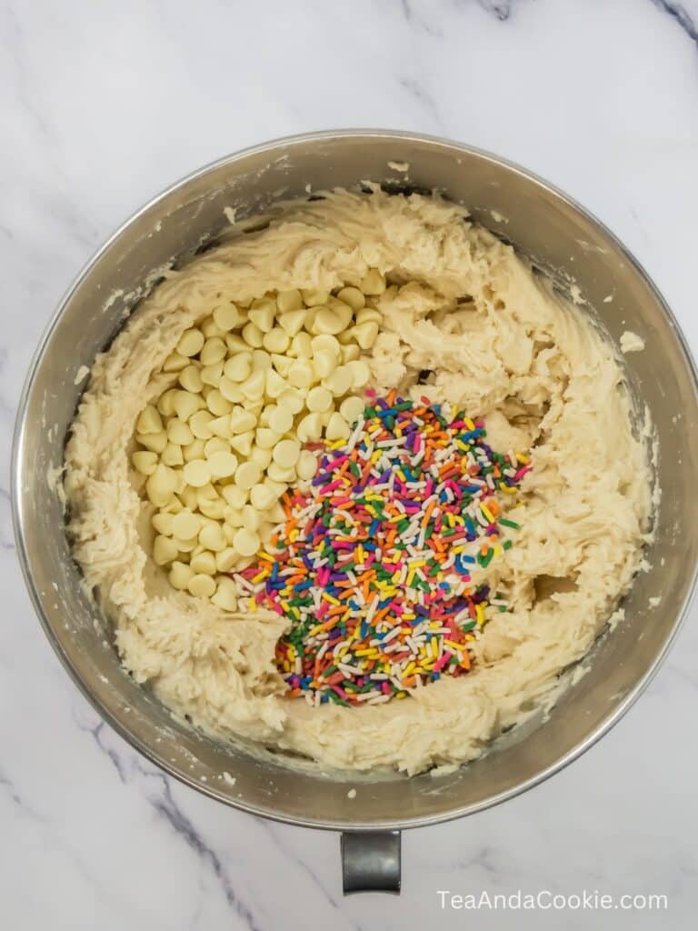 A bowl of cookie dough with sprinkles and white chocolate chips added on top to be mixed in