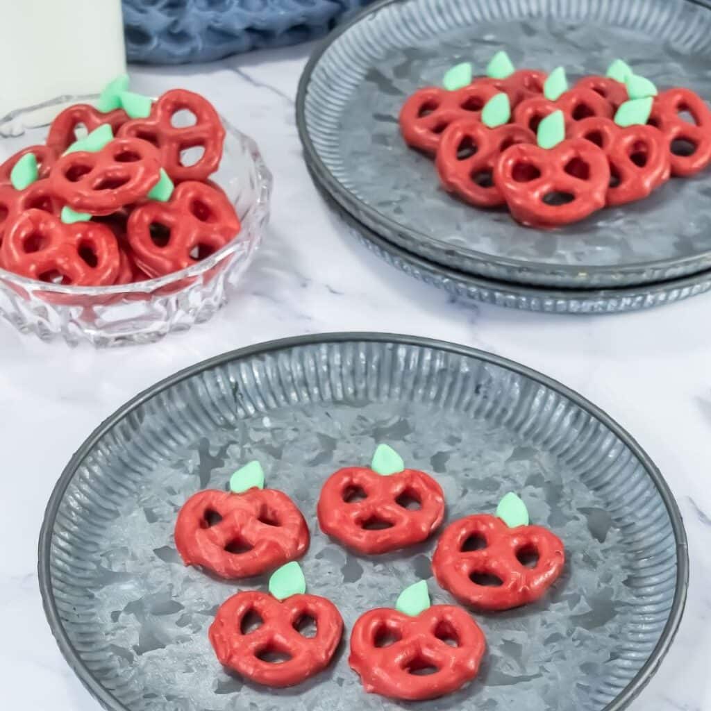 A plate of mini pretzel twists coated in red chocolate and decorated to look like an apple