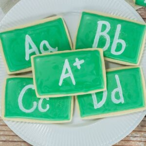 A plate of sugar cookies decorated with green icing and letters to look like a chalkboard