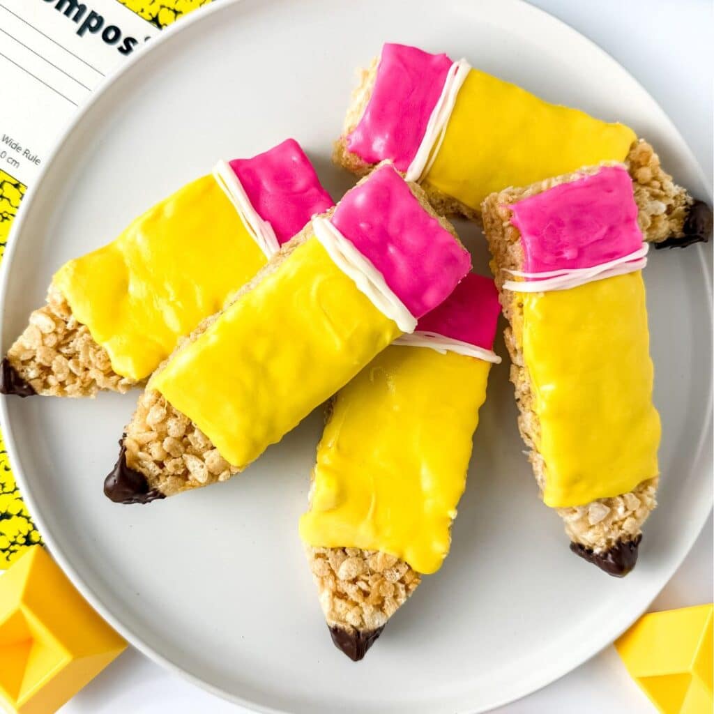 A plate with rice krispie treats cut and decorated to look like penciles, with yellow and pink melted chocolate