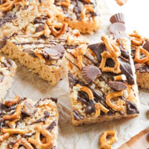 Parchment paper with peanut butter and chocolate rice krispy treats on top. There are mini Reese's and pretzels on top too