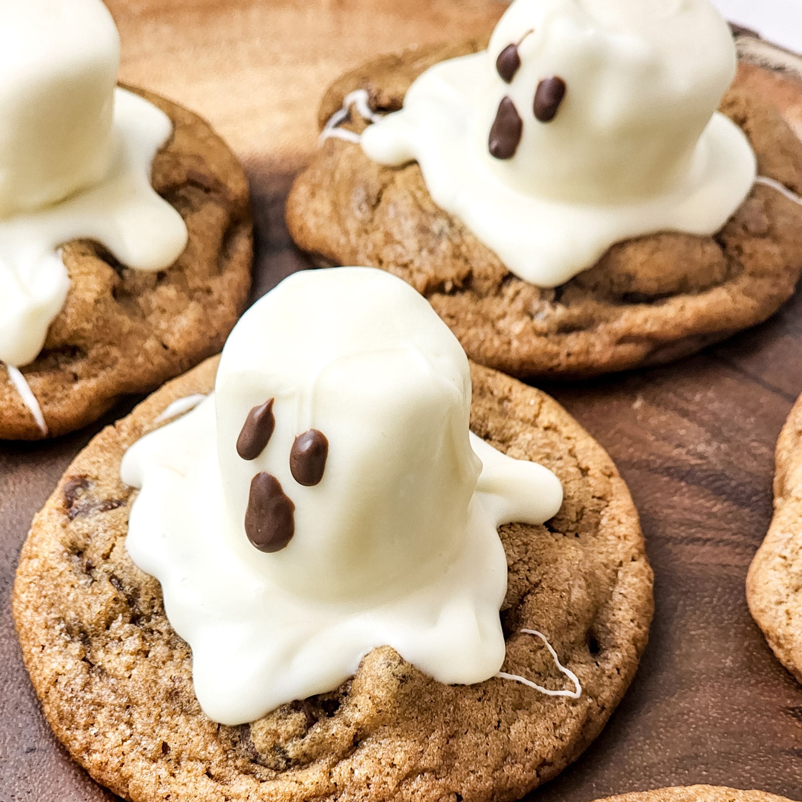 Cookies topped with marshmallows covered in white chocolate, decorated with chocolate faces to resemble ghosts.