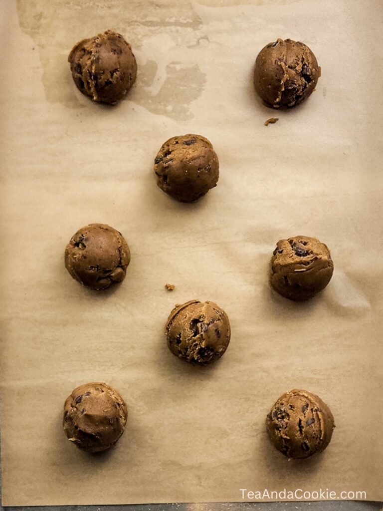 Eight scoops of chocolate chip cookie dough are arranged on a sheet of parchment paper, ready to be baked.