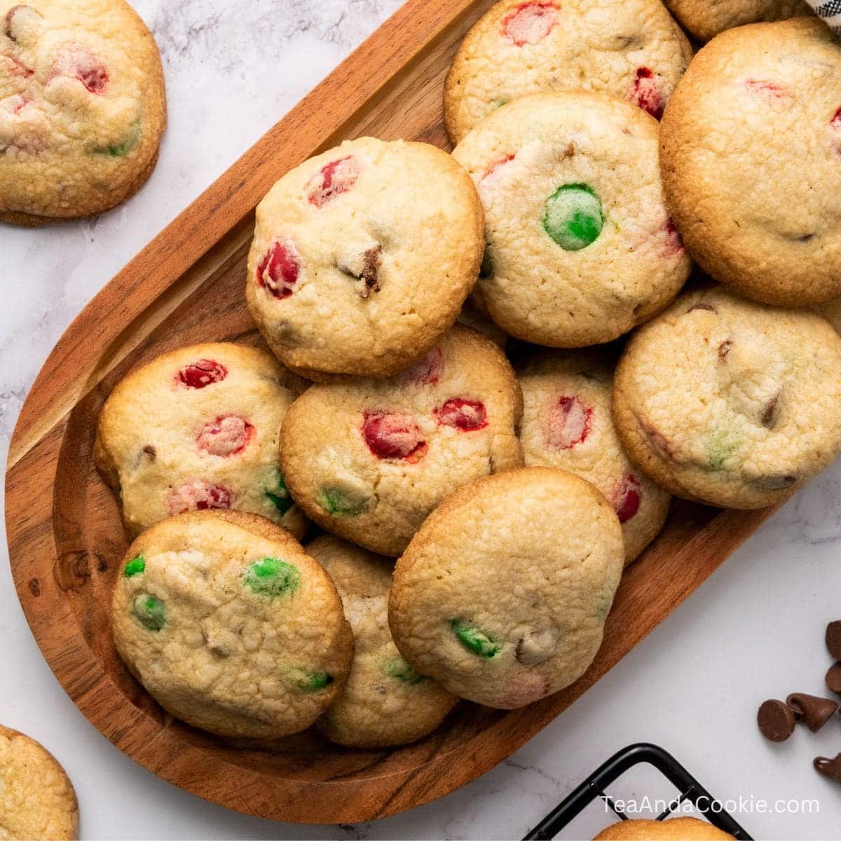MM Christmas Cookies. A wooden tray filled with cookies containing red and green candy pieces, placed on a white marble surface.