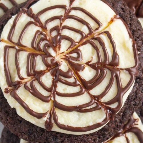Chocolate cookies topped with white icing and a chocolate spiderweb pattern, arranged in an overlapping stack on a white surface.