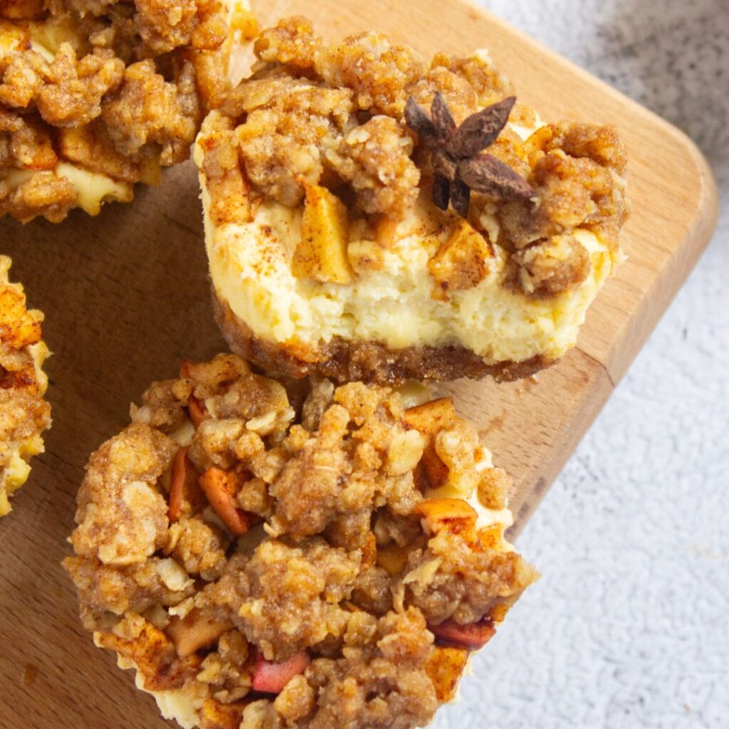 Apple crisp Mini cheesecakes topped with apple crumble and a star anise, arranged on a wooden board.