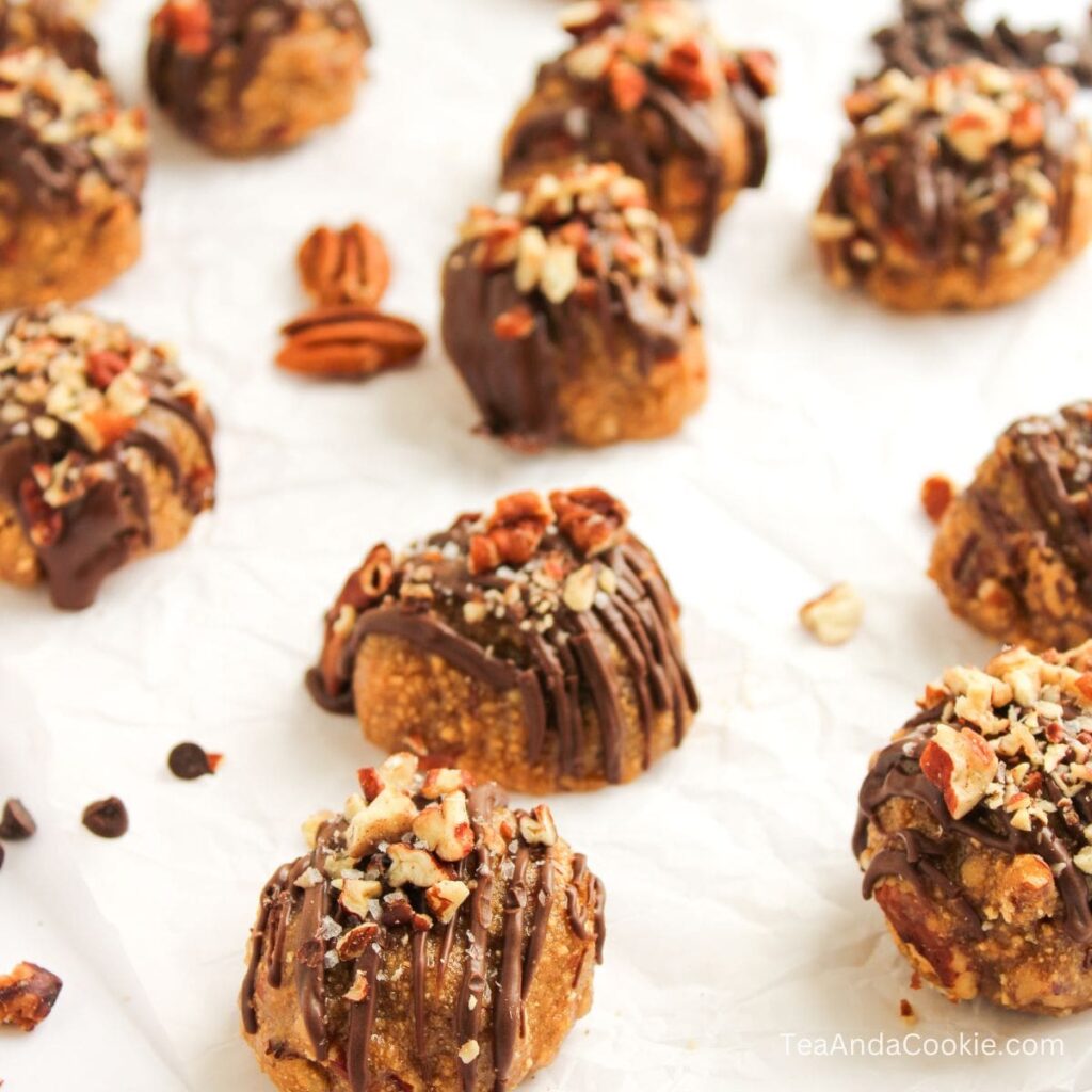 Easy Recipe for Pecan Pie Balls. No-bake cookies topped with chopped pecans and drizzled with chocolate, arranged on parchment paper with scattered chocolate chips and pecan halves.