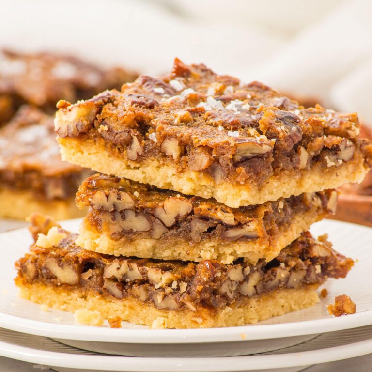 A stack of four pecan bars with a crumbly shortbread crust and nutty topping, placed on a white plate.