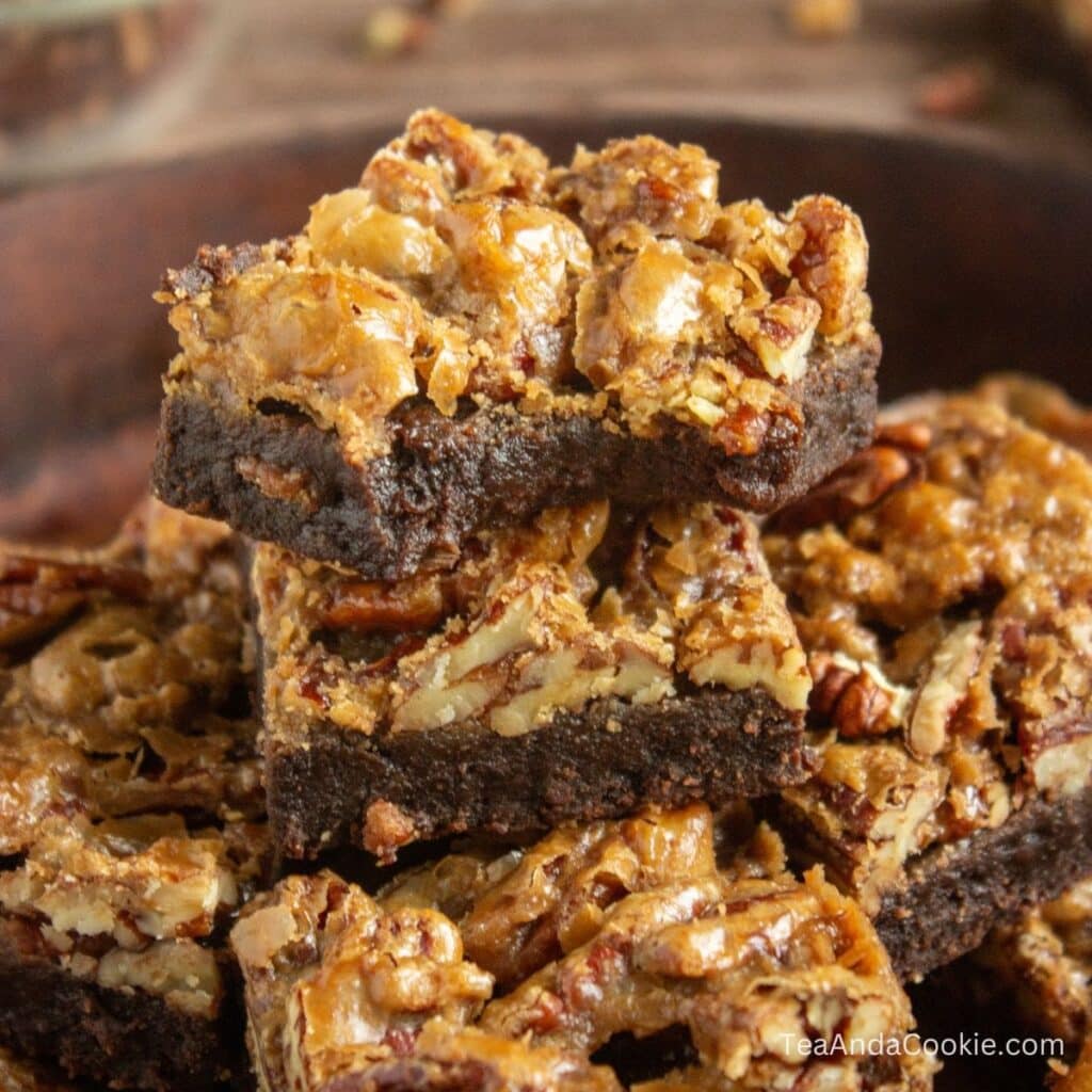 Pecan pie brownies recipe. Three stacked pecan brownies with a nut-filled topping are shown close up on a plate.