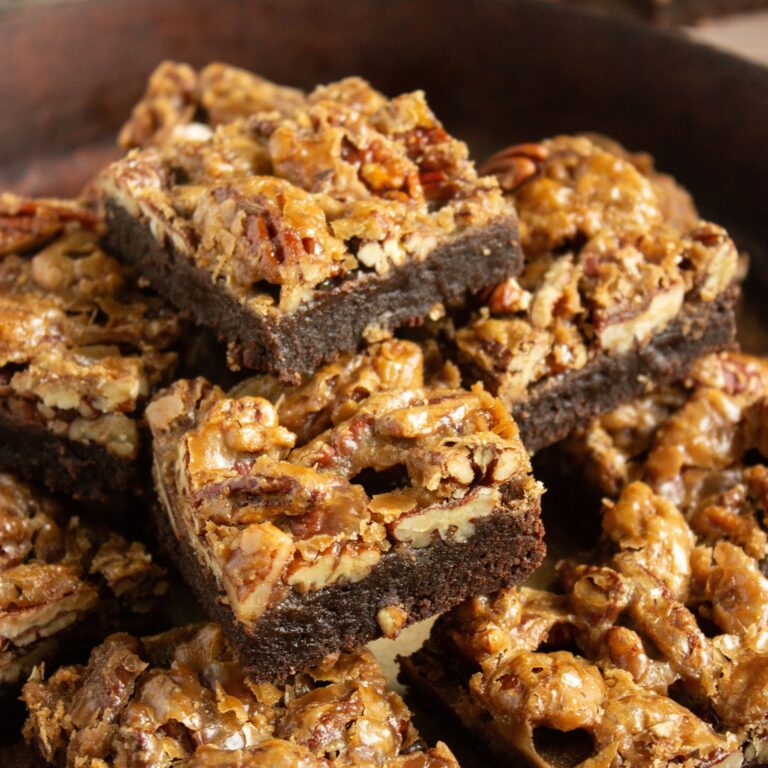 A close-up of a stack of dessert bars with a nutty, caramelized topping on a dark chocolate base.