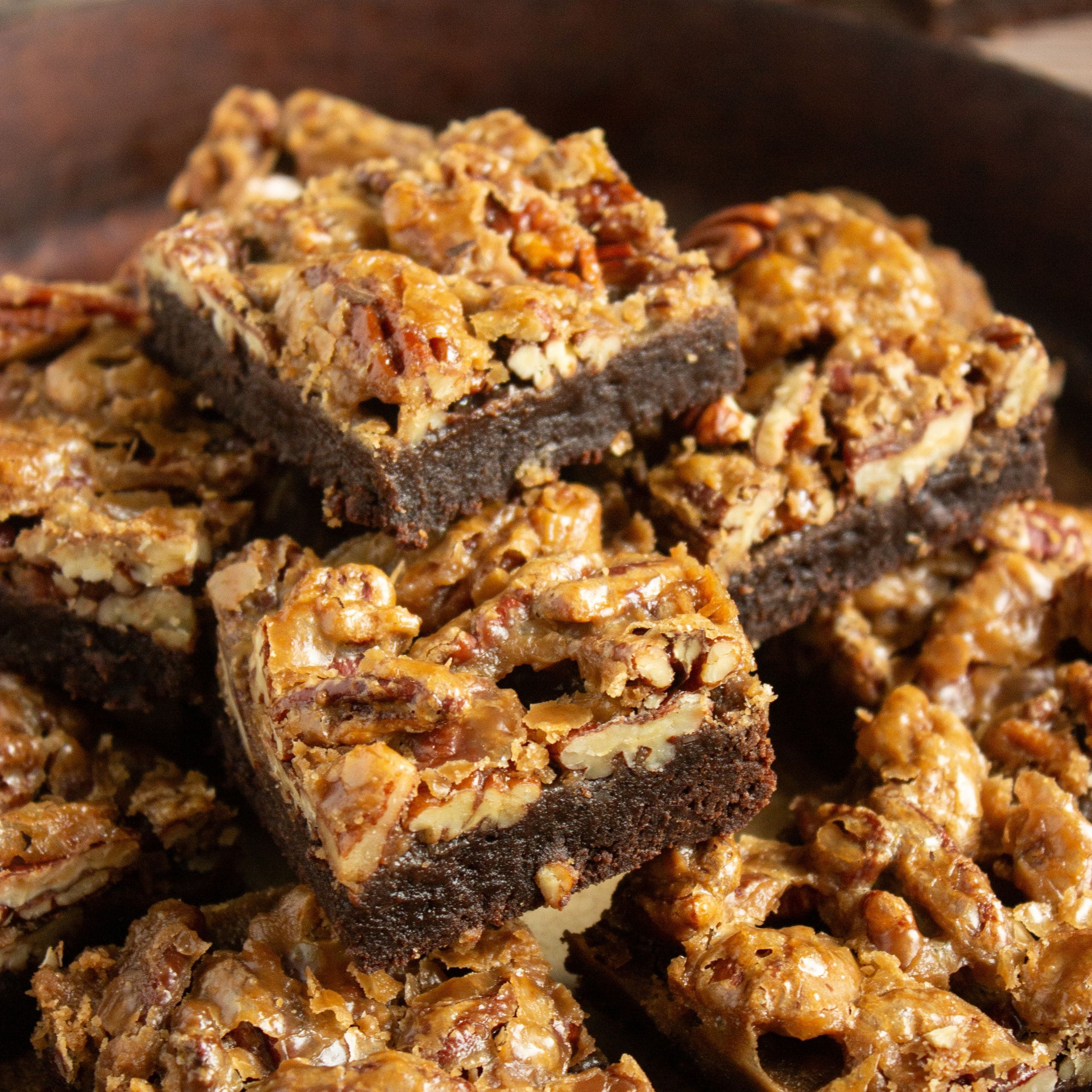 A close-up of a stack of dessert bars with a nutty, caramelized topping on a dark chocolate base.