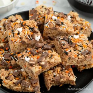 Rice Krispie treats with Halloween candy. A plate of rice crispy treats topped with chocolate chunks and Halloween-themed sprinkles in orange, white, and black.