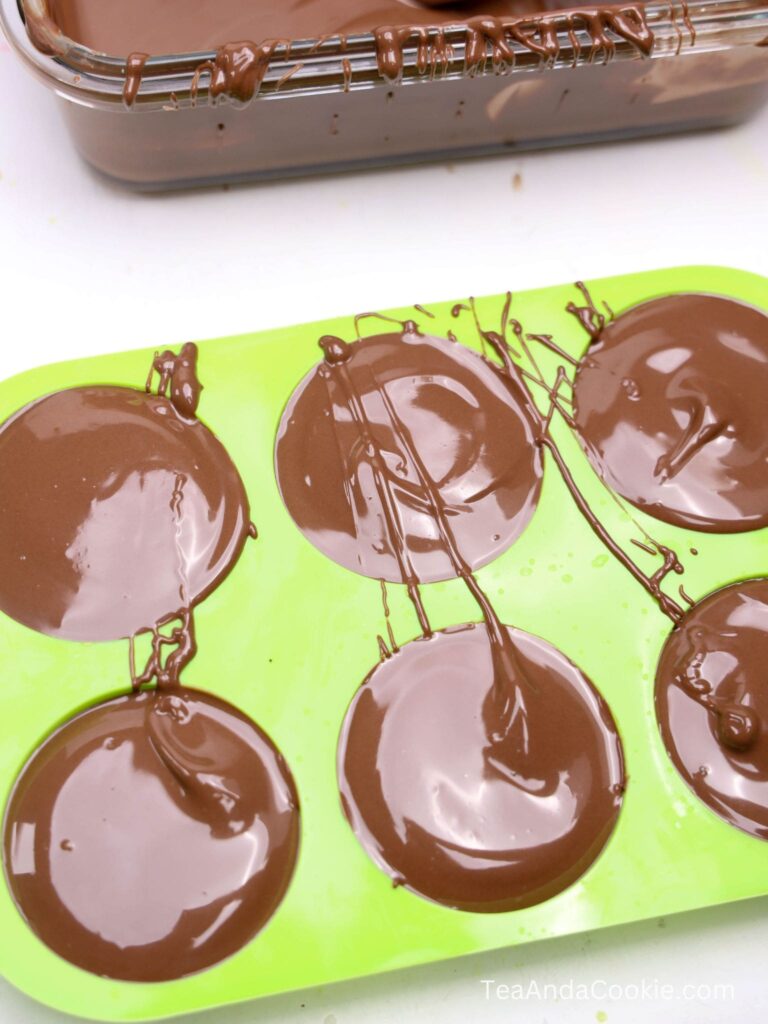 A green silicone mold filled with melted chocolate, next to a rectangular glass dish containing more chocolate.