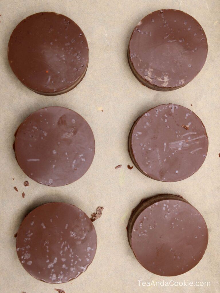 Six round chocolate-covered cookies are arranged in two vertical columns on a parchment-lined surface.