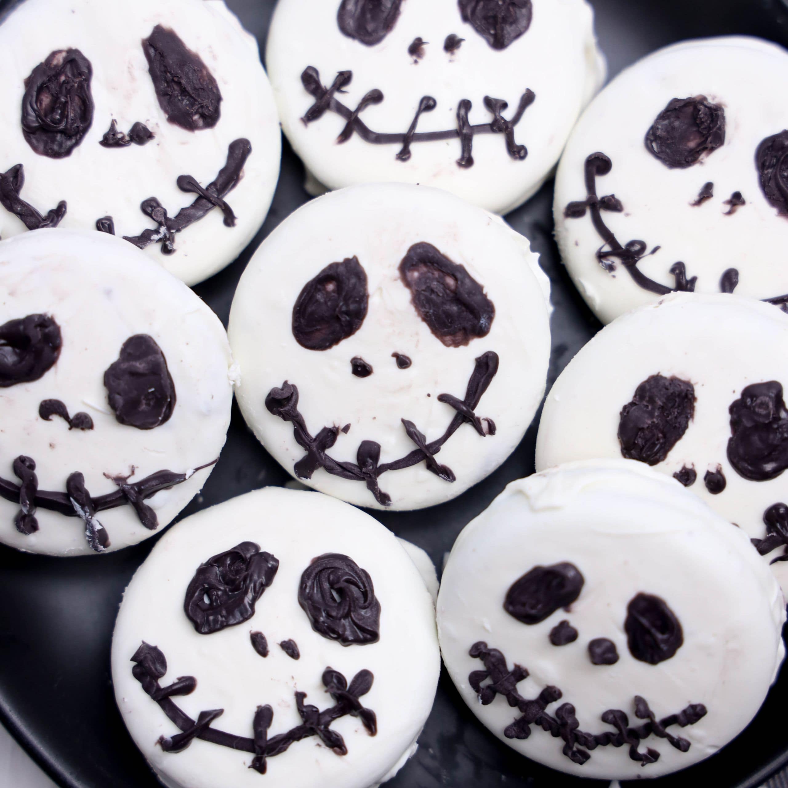 A plate of round cookies decorated with white icing and black icing faces resembling Jack Skellington from The Nightmare Before Christmas.