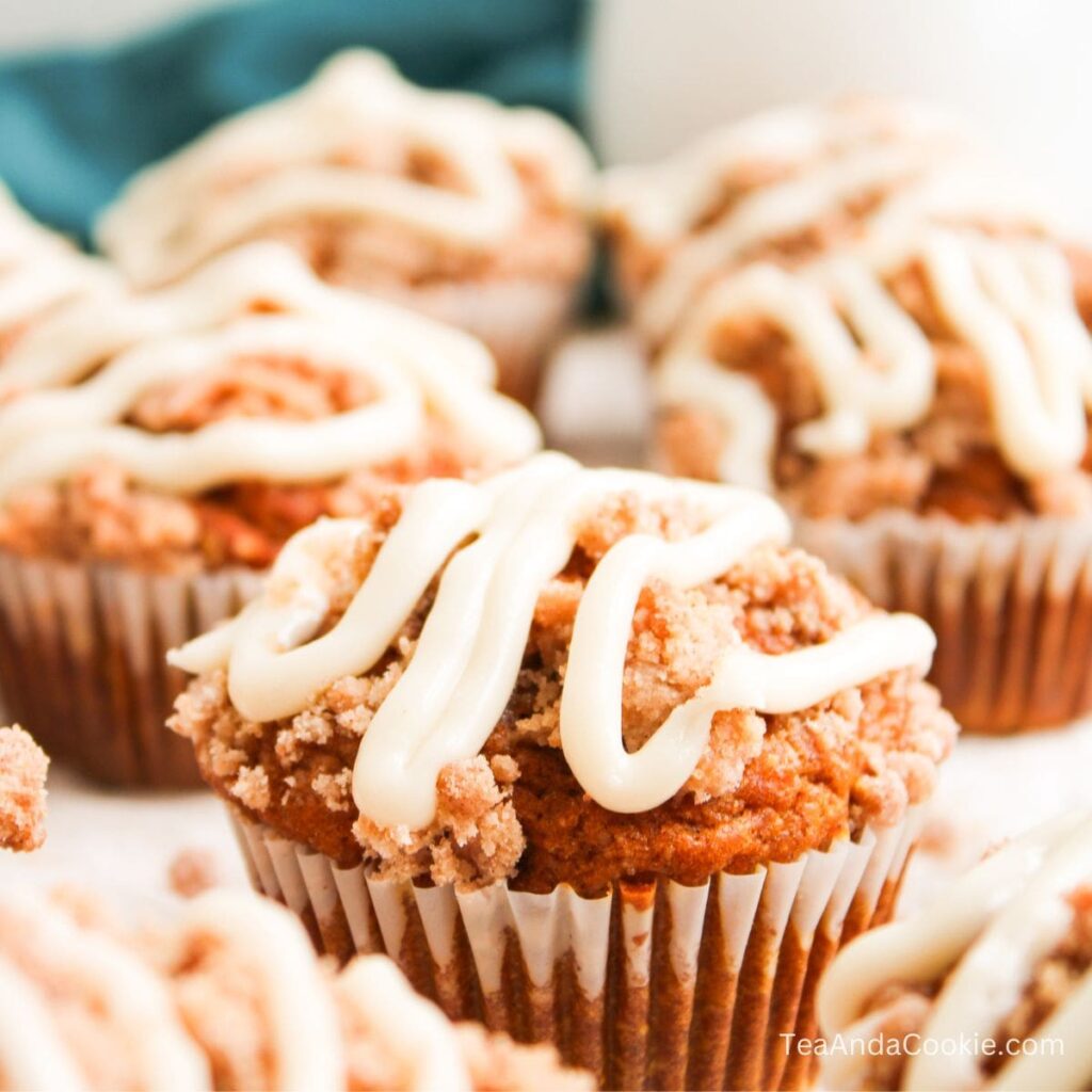 Pumpkin Muffins With Streusel Topping. A close-up of pumpkin streusel muffins topped with white icing, arranged on a white surface.