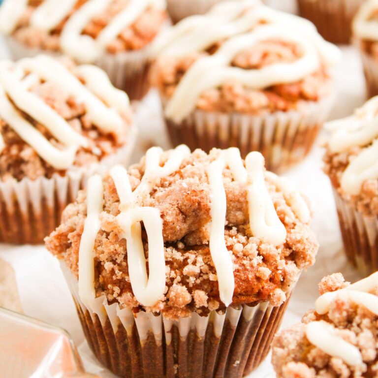 Pumpkin Muffins With Streusel Topping. Close-up of several muffins topped with crumbly streusel and drizzled white icing, arranged closely together on a white surface.