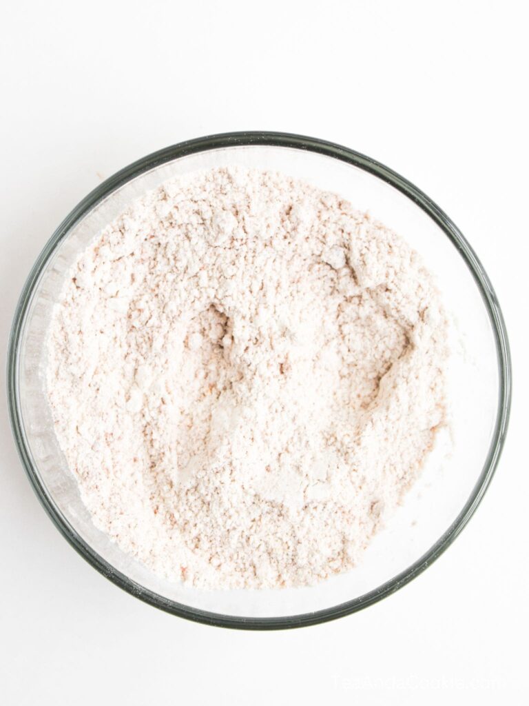 A clear glass bowl filled with a pale, finely ground powder, likely flour, on a white background.