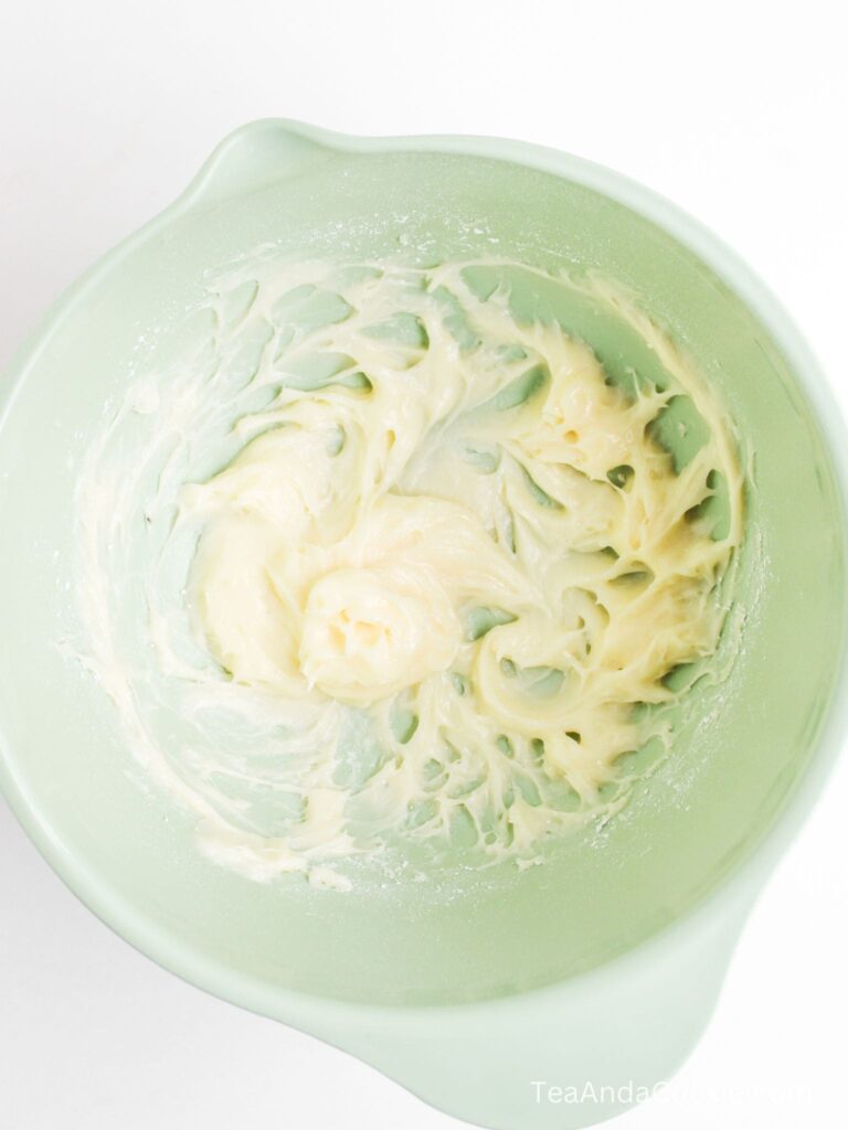 A pale green mixing bowl containing partially mixed creamy batter on a white surface.