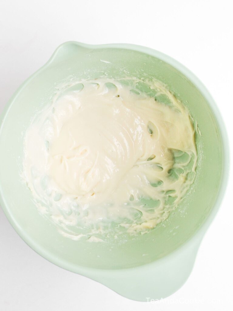 A light green mixing bowl filled with smooth, creamy batter or frosting sits on a white surface.
