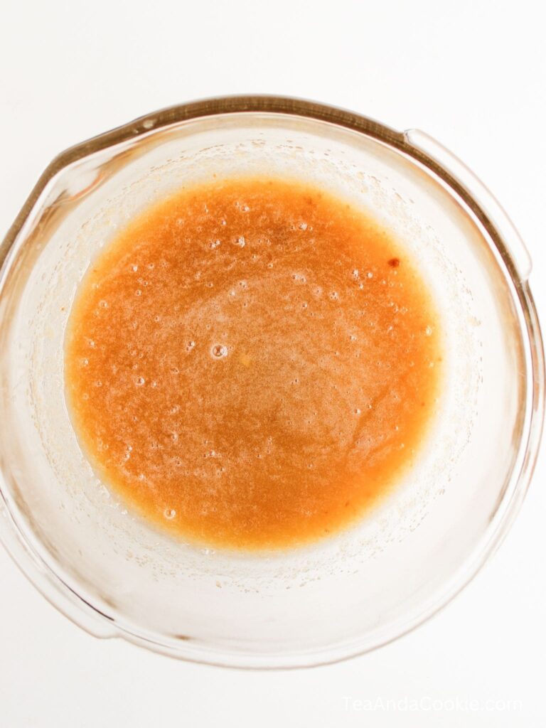 A glass bowl containing a light brown, frothy liquid mixture viewed from above.