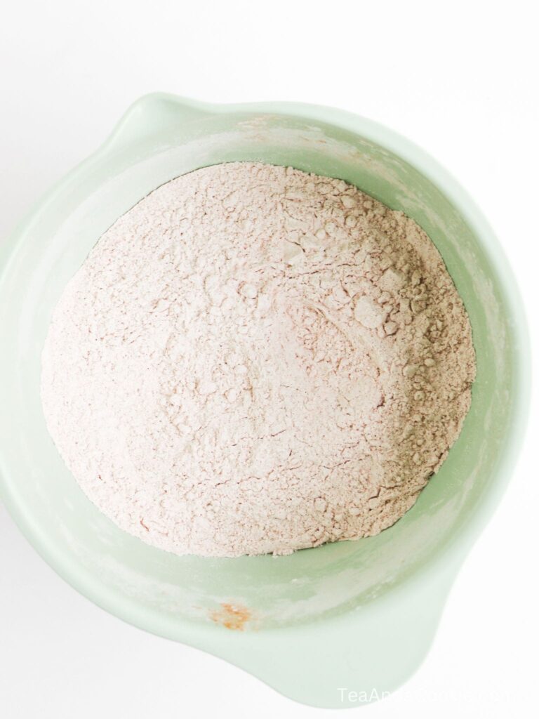 A green mixing bowl filled with a mound of dry, light brown or pinkish flour mixture, viewed from above.