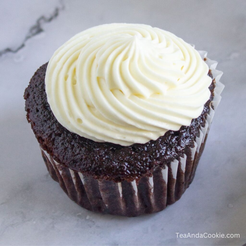 Chocolate Cupcakes With Sour Cream. A chocolate cupcake made with sour cream and topped with white swirled frosting sits on a light-colored surface.