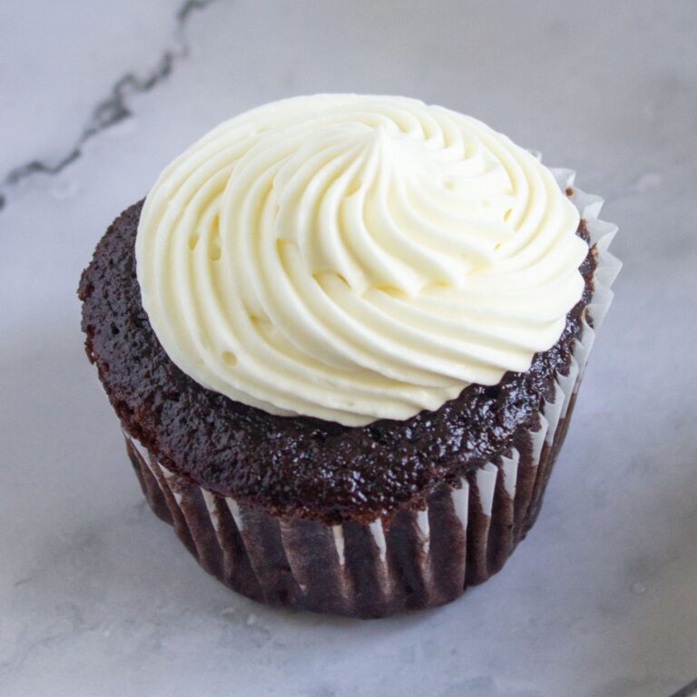 Chocolate cupcakes with sour cream topped with white swirled frosting on a marble surface.