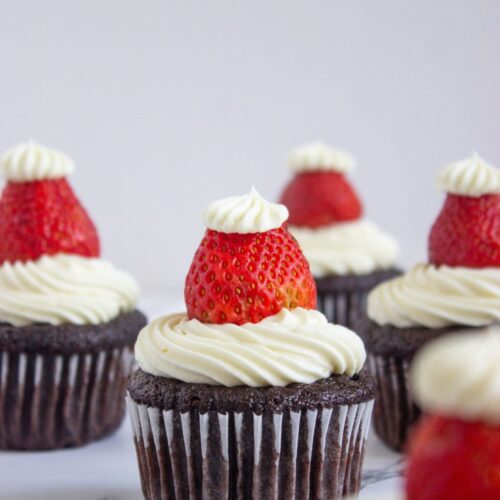 Chocolate cupcakes topped with swirls of white frosting, each decorated with a halved strawberry and a dollop of frosting on top.